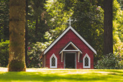 A small red church stands in a clearing of a forest.