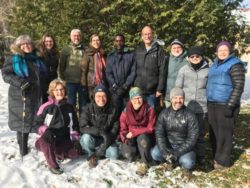 Doug Kaufman and a group of pastoral retreat participants pose for a group photo outside. There is still snow on the ground and all wear winter coats.