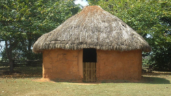 A small structure has a thatched roof and smooth mud walls. An opening faces us with a small wooden gate.